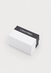 Scatola rettangolare bianca con una banda nera con il logo "Calvin Klein". Texture liscia, design chiuso e senza motivi visibili.
