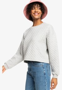 Light gray quilted sweatshirt with a cropped design, round neckline, and wide sleeves, paired with high-waisted blue jeans.