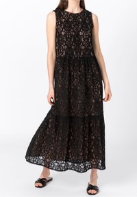 Černé krajkové maxi šaty s bezramínkovým designem, květinovými vzory a vrstevnatou sukní se zvlněným lemem. Nosené s černými sandály na klínku.