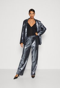 Třpytivý námořnický blazer s flitry a odpovídající kalhoty, které mají uvolněný střih a hladkou texturu. Černý bodysuit uvnitř a špičaté podpatky.