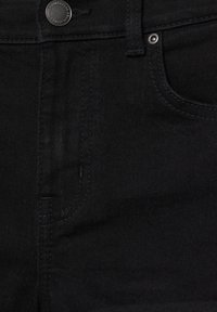 Gros plan sur un jean en denim noir, mettant l'accent sur le bouton, la fermeture éclair et les détails des coutures de la poche avant.