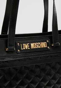 Black quilted handbag with gold "LOVE MOSCHINO" logo plaque, smooth leather accents, and sturdy double handles. Elegant texture and design.