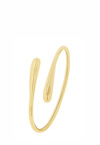 Pulsera de metal en tono dorado con un diseño fluido y ondulado, con dos extremos que se estrechan hacia puntos redondeados. Textura suave sin cierres visibles.