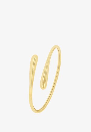 Pulsera de metal en tono dorado con un diseño fluido y ondulado, con dos extremos que se estrechan hacia puntos redondeados. Textura suave sin cierres visibles.