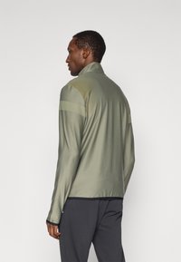 Αθλητικό μπουφάν σε ελαιοπράσινο χρώμα, από ελαφρύ ύφασμα, με ψηλό γιακά και υφασμάτινα πάνελ στους ώμους, διαθέτει μαύρη μπορντούρα και μανίκια.