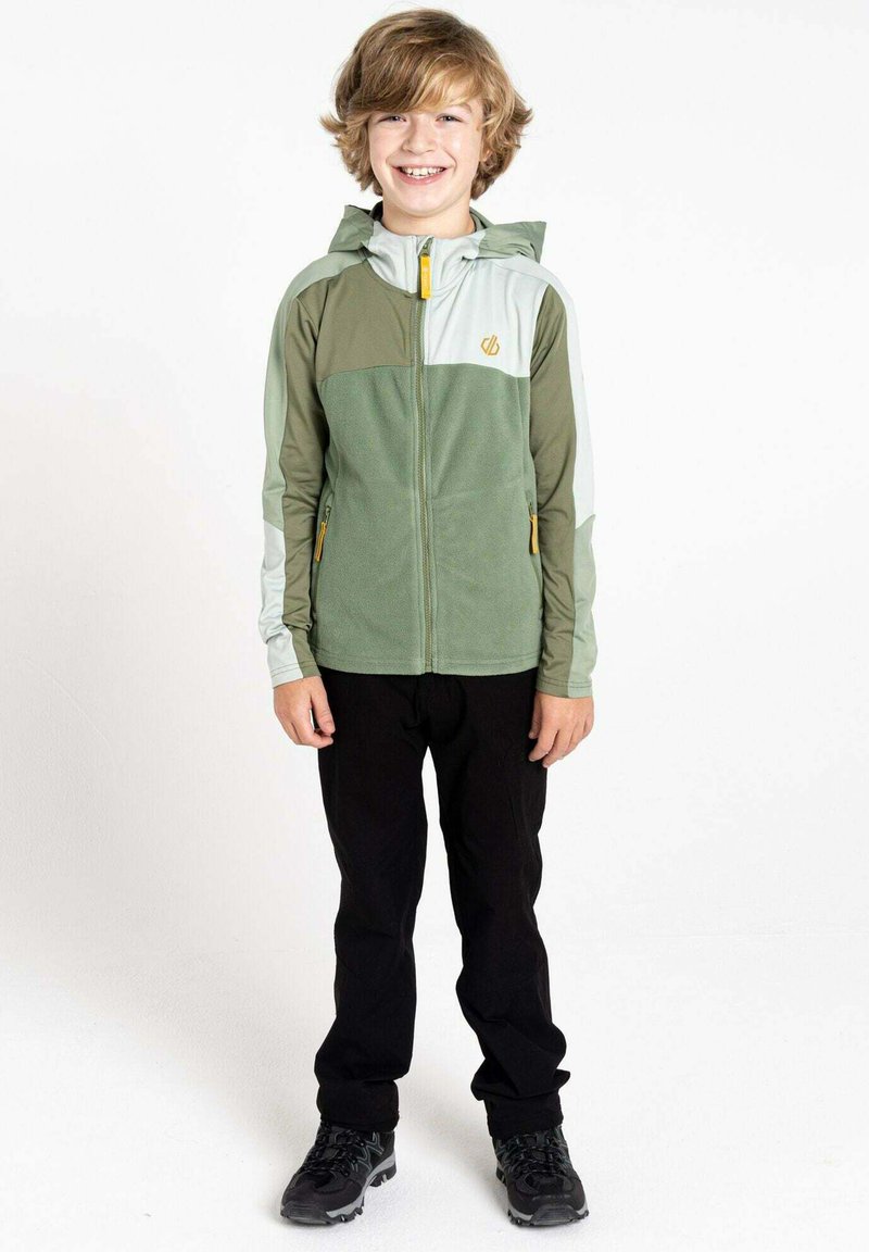 Grüne und graue zip-up Jacke mit Kapuze, ausgestattet mit strukturiertem Stoff, seitlichen Taschen und einem gelben Reißverschluss. Wird mit schwarzen Hosen und Schuhen getragen.