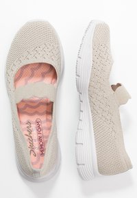 Zapato beige tipo slip-on con parte superior de punto que presenta un patrón transpirable. Suela blanca con agarre texturizado. La plantilla de espuma viscoelástica es visible.