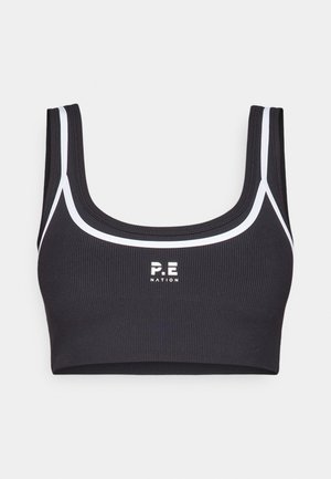 Musta ribattu urheiluhaalari valkoisilla saumoilla, neliön muotoinen pääntie ja "P.E NATION" -logo keskellä etuosaa. Käsittelee leveitä olkaimia ja joustavaa kangasta.
