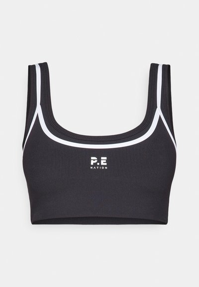 Musta ribattu urheiluhaalari valkoisilla saumoilla, neliön muotoinen pääntie ja "P.E NATION" -logo keskellä etuosaa. Käsittelee leveitä olkaimia ja joustavaa kangasta.