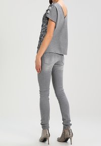 Šedý top s krátkým rukávem a květinovou aplikací na jednom rameni, spárovaný se slim-fit šedými džíny a metalickými kotníkovými botami na podpatku.