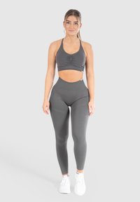 Grijs sportoutfit met een cropped top met geplooid detail en hoog aangesloten leggings, beide in een gladde, rekbare stof.
