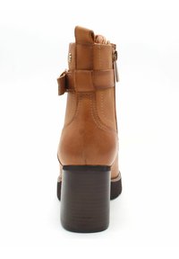 Brązowy skórzany botek za kostkę z blokowym obcasem, bocznym zamkiem błyskawicznym, dekoracyjnym paskiem i przeszyciami, widziany z tyłu.