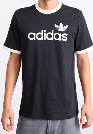 Black cotton t-shirt with white ribbed crew neck and sleeve hems. Features large white "adidas" logo and iconic trefoil on the chest.