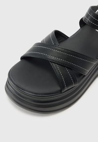 Sorte plattform sandaler med kryssdesign, laget av teksturert kunstskinn, med hvite sting og en glatt, polstret fotseng.