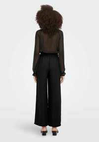 Haut noir à manches longues et transparent avec des points texturés, associé à un pantalon noir taille haute et large. Tissu lisse et détail de taille élastique.