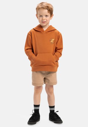 Sudadera naranja con un bolsillo frontal y detalles gráficos, combinada con pantalones cortos beige claros y zapatillas negras. Medias a rayas horizontales negras.