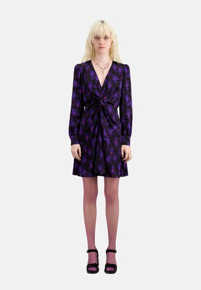 Vestido con estampado floral púrpura, de mangas largas y detalle de nudo en el frente, combinado con medias rosas y tacones negros con tiras.