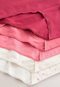 Stack of four women's cotton underwear in shades of red, pink, and white, with one pair featuring light pink polka dots.