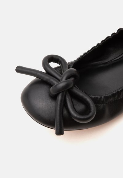 Ballerine plate en cuir noir avec des bords froncés et un grand nœud décoratif sur la partie arrondie des orteils.