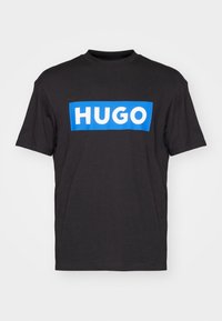 Schwarzes Baumwoll-T-Shirt mit kurzen Ärmeln, das ein blaues rechteckiges Logo mit weißem Text "HUGO" auf der Brust zeigt.