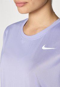 Camiseta deportiva corta de manga en color púrpura con escote redondo. Presenta un logo de Nike en blanco en el lado izquierdo del pecho y una textura suave y ligera.