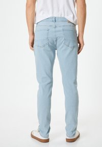 Jeans de mezclilla de color azul claro con un ajuste slim, que presentan bolsillos traseros y detalles de costura mínimos. Combinados con zapatillas blancas.
