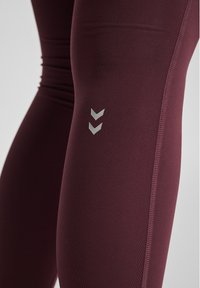 Mørkerøde leggings lavet af elastisk materiale. Har et sølvfarvet chevron-logo på låret og flade sømme for komfort. Glat tekstur.