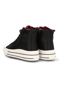 Zapatillas altas negras con suelas de goma blancas, cordones negros, cremallera lateral y forro interno rojo, mostradas desde ángulos trasero y lateral.
