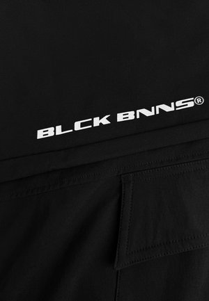 Zwarte textiel met een gladde textuur toont prominent de witte tekst "BLCK BNNS®". Het ontwerp is strak en minimalistisch.