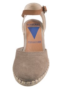 Sandalia de ante beige con punta redonda y suela de yute trenzado. Presenta una correa para el tobillo con hebilla. Etiquetada "VERBENAS, 100% HECHO EN ESPAÑA."