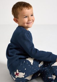 Marineblå skjorte med lange ærmer parret med mønstrede leggings med isbjørne og snefnug på en mørkeblå baggrund.