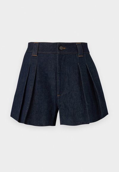 Σκούρες μπλε πλισέ τζιν σορτς με θηλιές για ζώνη, κουμπί στο μπροστινό μέρος και κλείσιμο με φερμουάρ σε ανοιχτό γκρι φόντο.