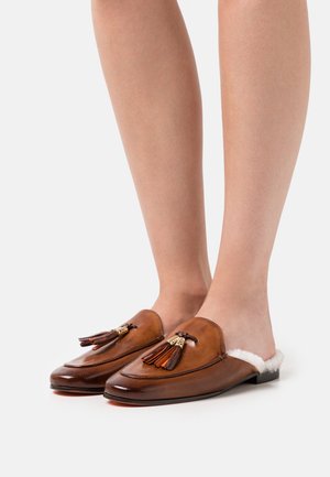 Chaussures en cuir marron à enfiler avec une doublure blanche douce, ornées de pampilles décoratives et d'une finition brillante. Semelles plates et bouts arrondis.