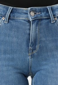 Blå denimjeans har en klassisk passform med dragkedja och metalldetalj för stängning. De har en slät textur och synliga sömdetaljer.