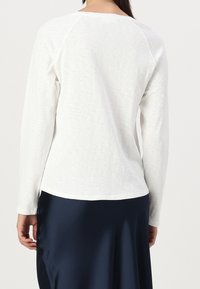 Camicia bianca a maniche lunghe con una finitura testurizzata, caratterizzata da un collo rotondo e maniche raglan. Abbinata a una gonna di raso blu navy.