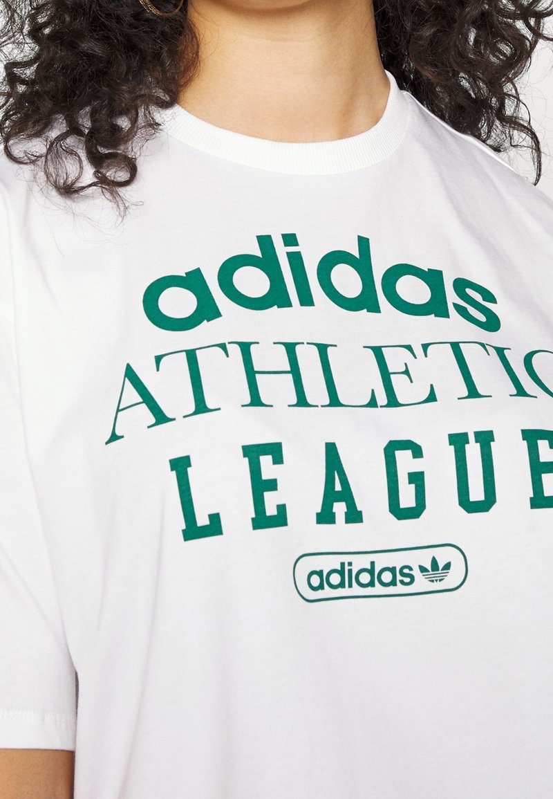 Vit kortärmad t-shirt med grön text som står "adidas ATHLETIC LEAGUE" och logotyp. Mjuk bomullstyp, rundad halsringning, avslappnad passform.