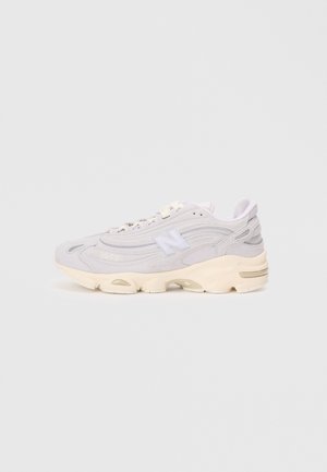 Biały i jasnoszary sneaker New Balance z masywną kremową podeszwą, sznurowanym zapięciem i logo "N" na boku, widoczny z profilu na białym tle.