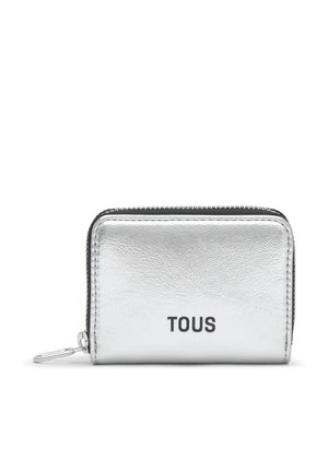 Una pequeña cartera plateada TOUS con cremallera alrededor, acabado texturizado y un llavero metálico, sobre un fondo blanco.