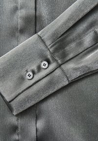 Grijs satijnen overhemddetail met een omgevouwen manchet en twee knoopsluitingen, dat een gladde textuur en subtiele glans toont.