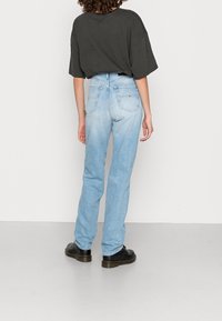 Ljust blå denimjeans med rak passform, hög midja och bakfickor. Bärs med en lös svart t-shirt och svarta skor.