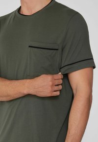 Camiseta de manga corta verde oscuro con un bolsillo con ribete negro. Tela suave, cuello redondo y diseño ligeramente ajustado.