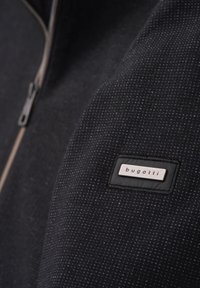 Schwarze strukturierte Jacke mit silbernem Reißverschluss und einem gestickten Bugatti-Logo auf einem rechteckigen Patch. Verfügt über ein dezentes Punktmuster.