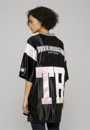 Zwarte satijnen jersey met witte en roze accenten, met het "TRUE RELIGION"-logo en een grote "TB" op de achterkant, korte mouwen en een gestreepte kraag.