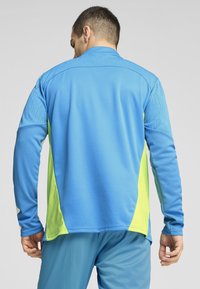 Langarm sportshirt in blauw en helder groen, met textuur op de mouwen, een kraag en een zoom die aan de zijkanten lichtjes rondloopt.