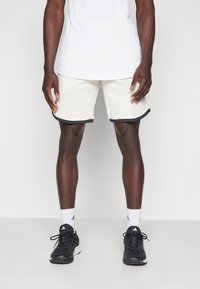 Light-colored athletic shorts with a black trim, paired with black shoes and white socks. Material appears smooth with a relaxed fit.