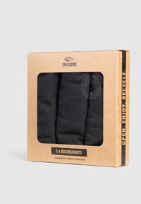 Svarta boxershorts förpackade i en transparent fönsterlåda. Kartongförpackningen har bruna och svarta färger med "Smilodox"-logotyp och återvinningsinstruktioner.