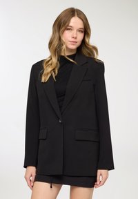 Blazer nero con design strutturato, chiusura a un solo bottone, due tasche frontali e texture liscia. Presenta rever sagomati e una vestibilità comoda.