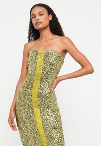 Sárga flitteres ruha pánt nélküli kialakítással, középen selyem panelel és díszgombokkal az elején, testhezálló fazon.