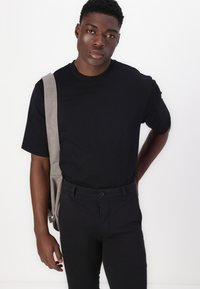 Black short-sleeve t-shirt made of cotton, paired with black pants. A gray shoulder bag is draped over one shoulder.
