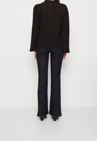 Svart långärmad blus med samlad axeldetalj, i kombination med mörka utsvängda jeans. Klackar kompletterar outfiten. Enkelt och elegant design.